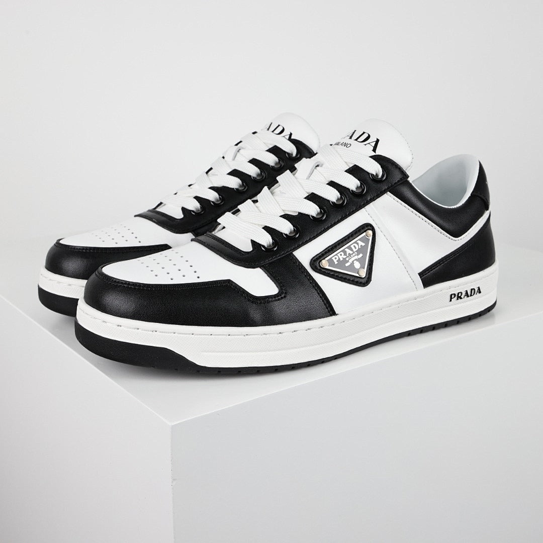 Black-and-white low-top sneakers with white laces, a triangular side plaque, and a white midsole.